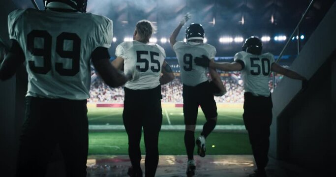 American Football Players Entering a Packed Stadium Through the Tunnel. Diverse Team of Four Footballers Standing on a Green Field, Raising Arms, Motivating Emotional Sports Fans