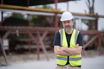 Senior White engineer cross arm at chest looking at camera with smile at work site. Portrait og engineer wearing white hard hat at manufactuing.