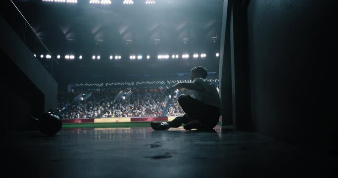 American Football Player Sitting Down Alone in Stadium Tunnel. Male Athlete Reflects on Championship Game, Feeling Sad and Stressed After a Loss. Emotional Strain Moment in Professional Sport