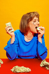 Portrait of young girl with makeup holding dollar money, crying and eating onion against vivid...