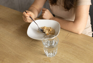 young woman holds a spoon with oatmeal, a glass of water
