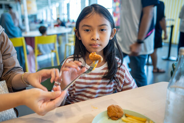 Asian little girl eating a chicken nugget