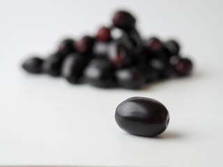 One Java plum fruit in front of Java plums group on white background.