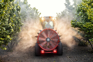 Agricultural sprayer machine with large fan spraying and cultivating orchard with fertilizer.