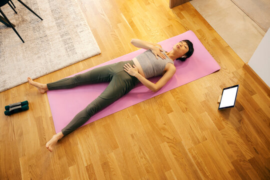 A middle aged japanese woman is lying down on yoga mat and practicing breathing.
