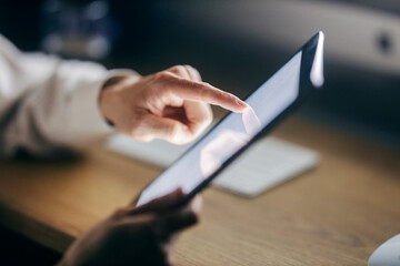 Close up of female's hand scrolling on tablet in dark room.