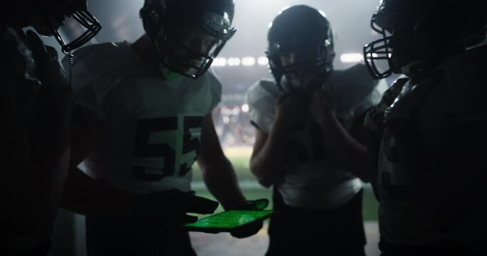 Football Stadium Tunnel: Group of Athletic American Football Players Planning Game Strategy on a Tablet Computer Before a Championship Match. Crowd of Spectators Cheering in the Background