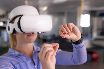 Caucasian female therapist in VR headset gestures at gym rehabilitation center