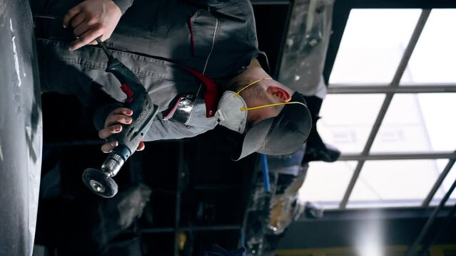 vertical video at a service station a car mechanic is trying to sand part of the car