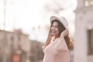 A woman wearing a white hat and a pink shirt is smiling and posing for a picture. The image has a warm and cheerful mood, with the woman's smile and the bright colors of her outfit.