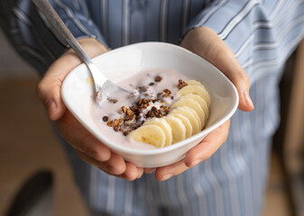 female hands, plate with granola, yogurt and bananas, top view