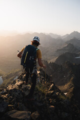 Obraz premium Young mountaineer with a backpack walking along a rocky ridge in the Pyrenees while climbing or mountaineering at sunrise