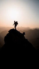 Mountaineer on the summit of a rock pinnacle backlit at sunrise in the Pyrenees