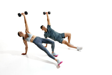 Athletic man and woman performing challenging exercise with dumbbells demonstrate strength and balance against white background. Concept of people in sport, healthy lifestyle, teamwork, motivation.