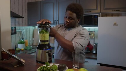 African American man with obesity using kitchen blender while preparing healthy green smoothie for weight loss at home - Powered by Adobe