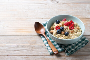 Oatmeal porridge with raspberries, blueberries and almonds in bowl on wooden table. Copy space