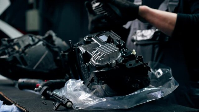 close up At a service station an auto mechanic unscrews the bolts in the headlight in part of the car to get to the inside