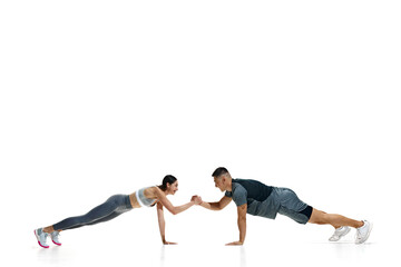 Obraz premium Man and woman in plank position, in friendly arm wrestling match while maintaining their balance against white studio background. Concept of people in sport, healthy lifestyle, teamwork, motivation.