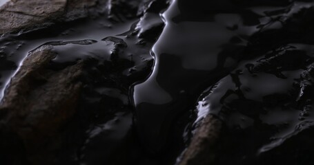 Glossy Oil Flowing on Rocky Shore. Close-up, shallow dof.