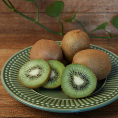 Whole and cut kiwis inside a green plate on a wooden background