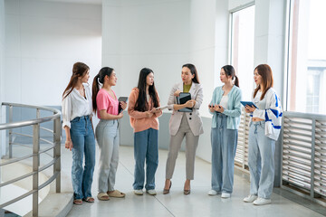 A group of women are standing together in a hallway, some of them holding books
