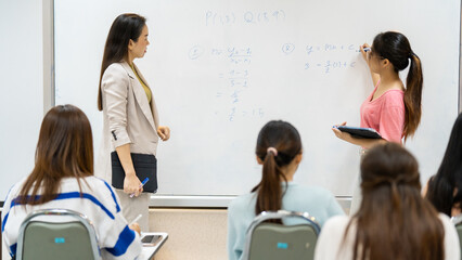 A teacher is writing on a whiteboard in front of a group of students