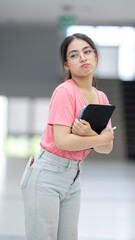 A woman in a pink shirt and jeans is holding a book and a pen