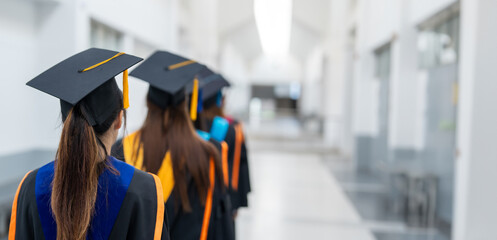 A group of women wearing graduation caps and gowns walk down a hallway