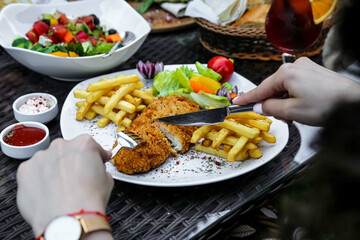 Person Cutting Chicken and French Fries on a Plate