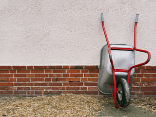 Hay surrounding metal wheelbarrow leaning against wall
