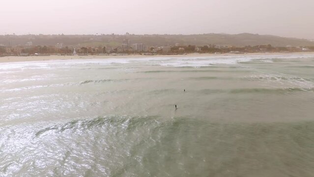 Surfers waiting for waves in Giulianova sandy beach close to the port at misty day. Drone orbit shot.
