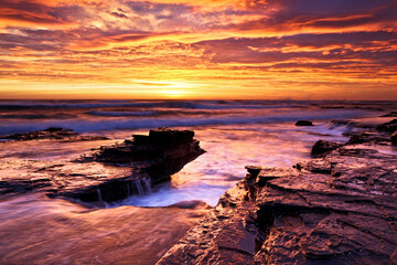 Long exposure of a vibrant orange sunrise over a rocky coastline