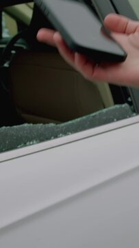Close-up hand holding phone upon seeing shattered car window dialing 112 immediate emergency assistance vertical video. Hand grabs phone dialing 112 broken auto glass reacting promptly to situation.