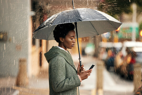 Black woman, phone and umbrella with rain in city for communication, walk and travel to work. African girl, smartphone and protection from winter weather for internet, email and business update