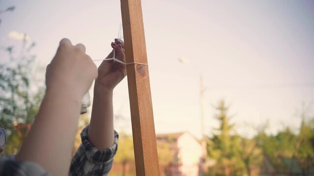 a woman ties ropes around a frame for a grape bush
