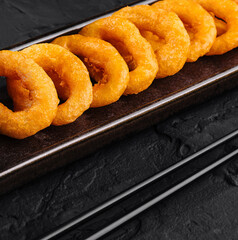 Crispy fried onion rings with dipping sauce on dark background
