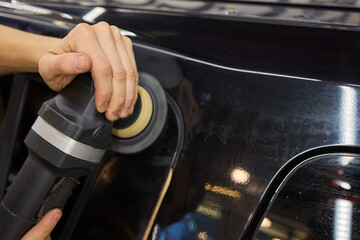Obraz premium Person using machine to polish black cars automotive exterior