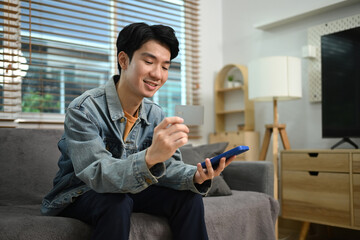 Handsome asian man holding a credit card and purchasing online on smartphone