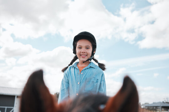 Portrait, child and riding horse in countryside on farm ranch for horseback learning, activity and helmet for safety in summer. Smile, girl and animal on field for lessons as childhood sport for race