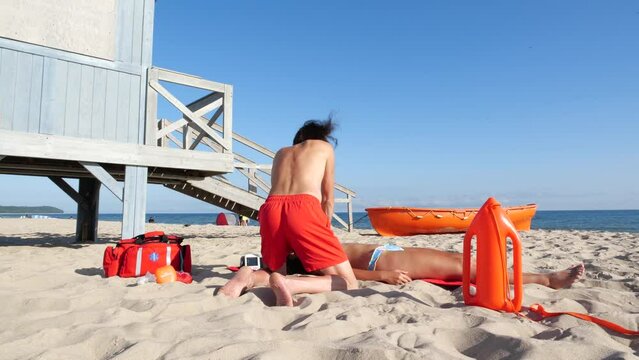 Rescue and resuscitation of unconscious drowning victim, young woman. A lifeguard performs cardiopulmonary resuscitation  against the background of lifeguard tower at the beach in summer time.