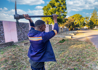 african worker with a pickaxe digging the soil in the street