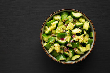 Homemade Smashed Cucumber Salad in a Bowl on a black background, top view. Space for text.