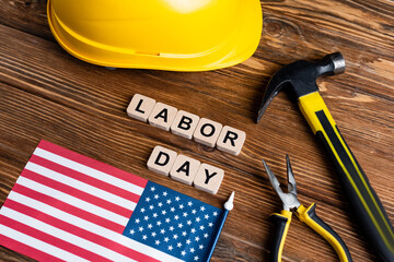 usa flag, hammer, pliers, hardhat and cubes with labor day lettering on wooden table