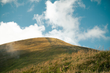 A grassy hill under a blue sky with scattered clouds
