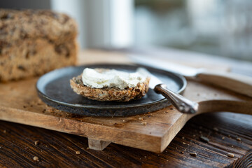 Fresh whole grain bread with cream cheese and dark plate on a wooden cuttingboard. Close-up with...