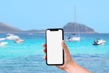 Hand holds mobile phone screen against of turquoise sea with yachts background