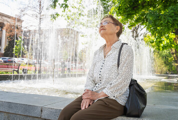 Senior happy attractive woman enjoying fresh air in the park near the fountain