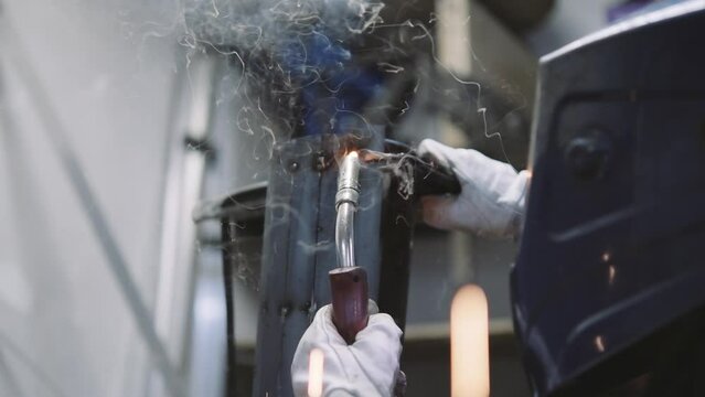 Close-up shot of the artisan welding a metal piece in the workshop, creating a piece of art metal.
