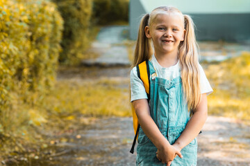 Cute smiling little girl with backpack on a greenery background. Education concept. First grader...