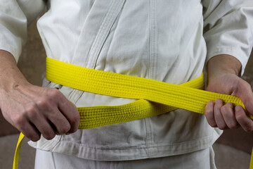 Kyokushinkai karate athlete ties yellow belt around his waist, adjusting martial arts equipment,...